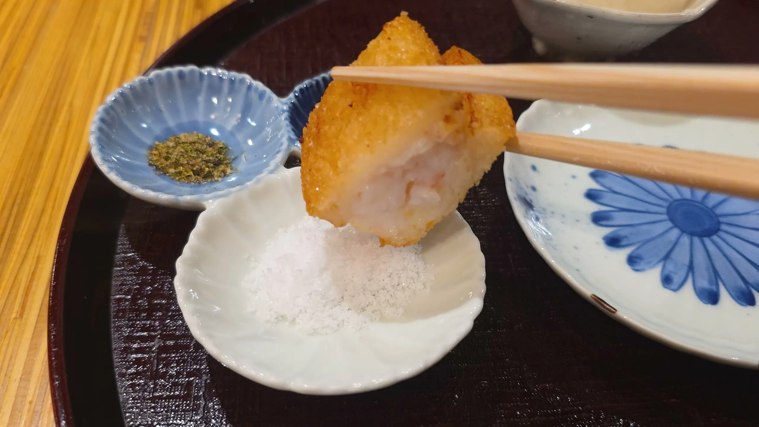 Hatoshi shrimp toast held in chopsticks over dishes of salt and green seasoning