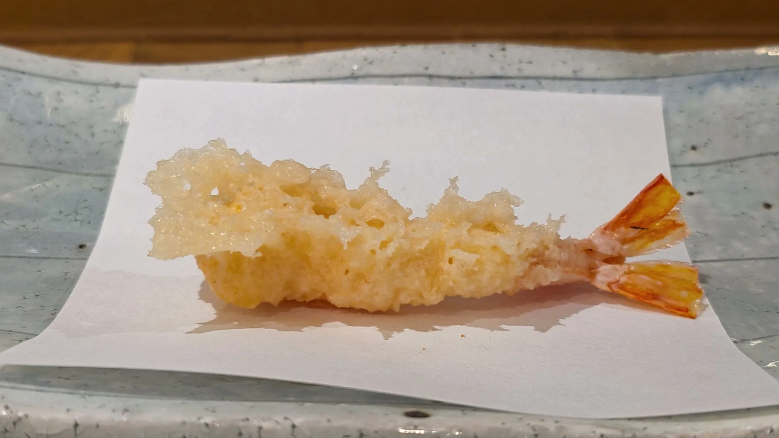 Kuruma-ebi tempura with a lacy, cratered batter and its tail on white paper at Tempura Asanuma