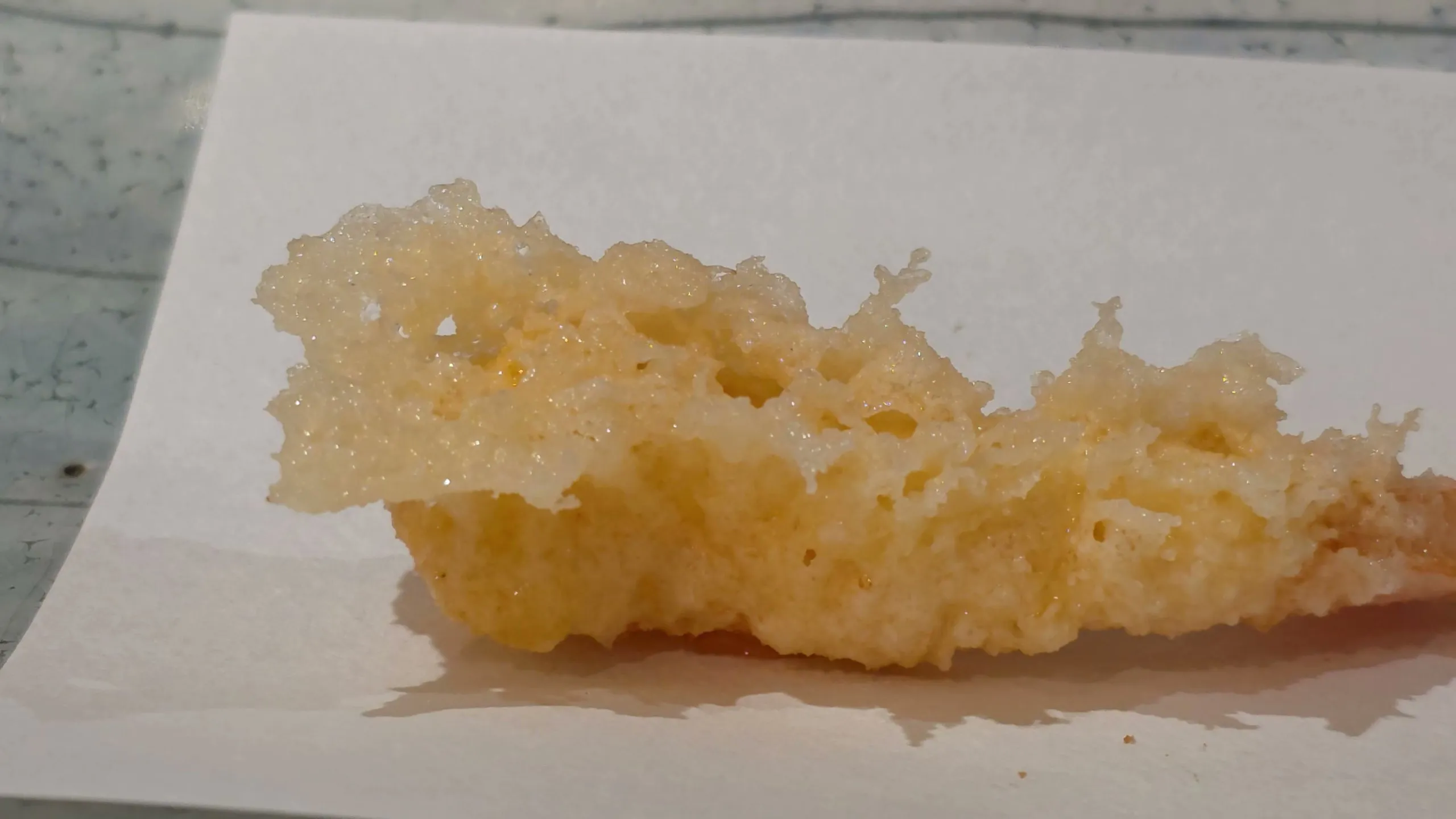 Close-up of kuruma-ebi tempura with a lacy, cratered batter on white paper