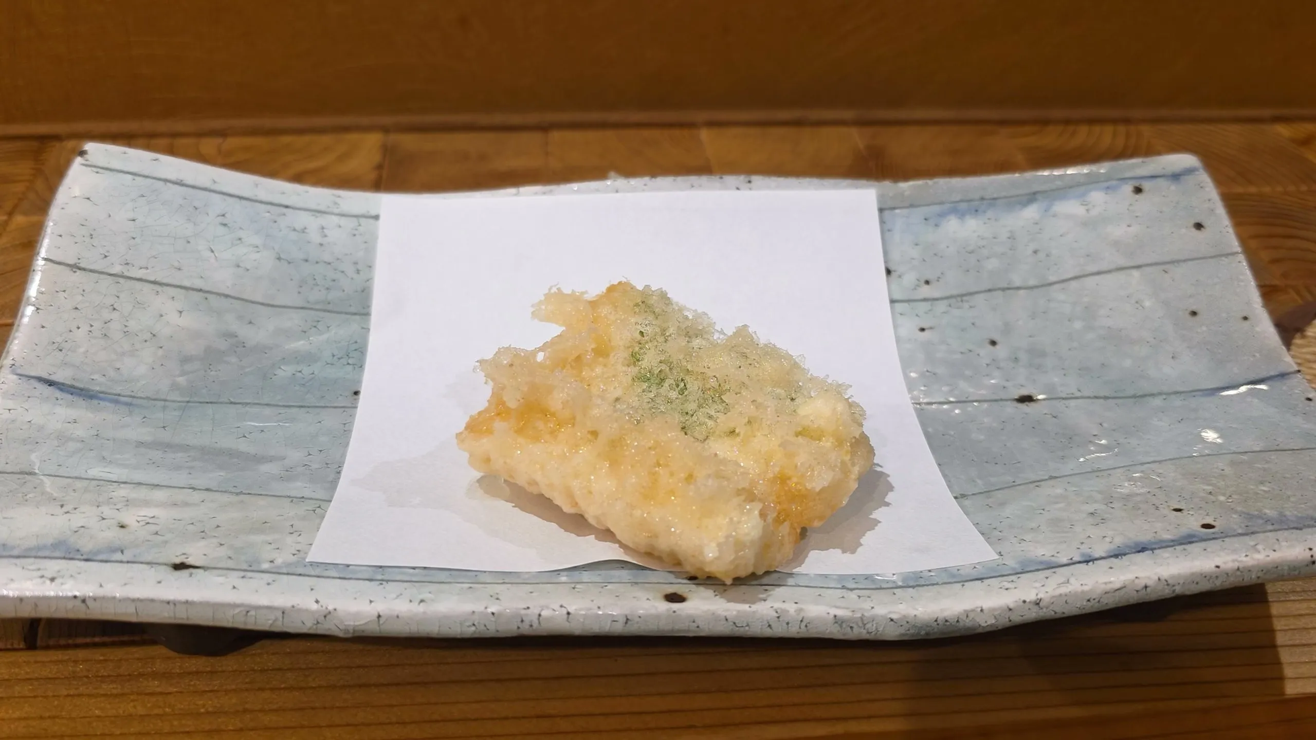 Hairtail tempura with shiso and a sprinkle of green on white paper