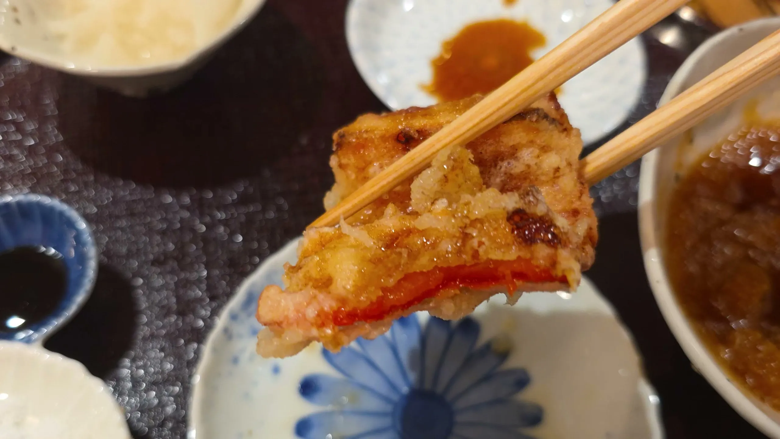 Red bell pepper tempura held in chopsticks, the pepper showing under the coating
